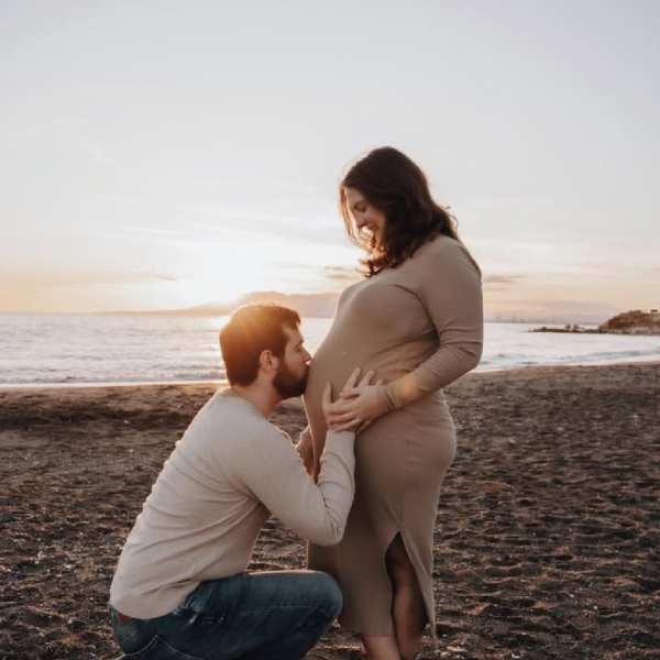 Een hoogzwangere Jenna en haar man bij zonsondergang op het strand in Spanje